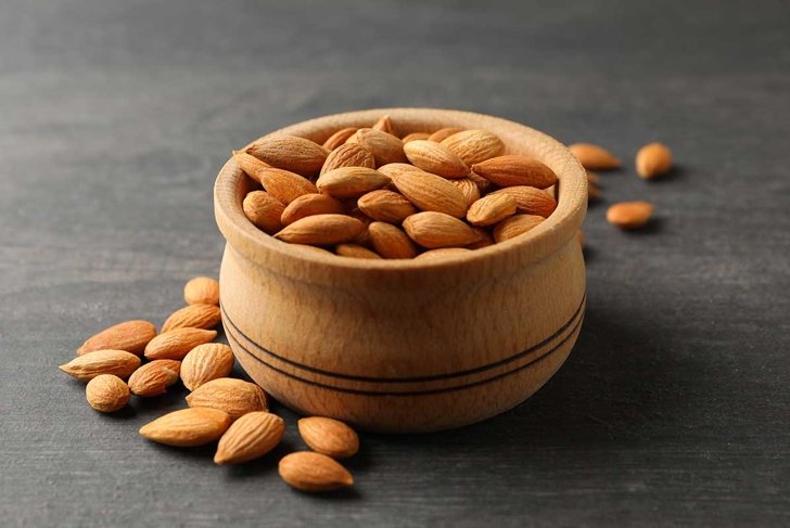Bowl with tasty almond on gray wooden background